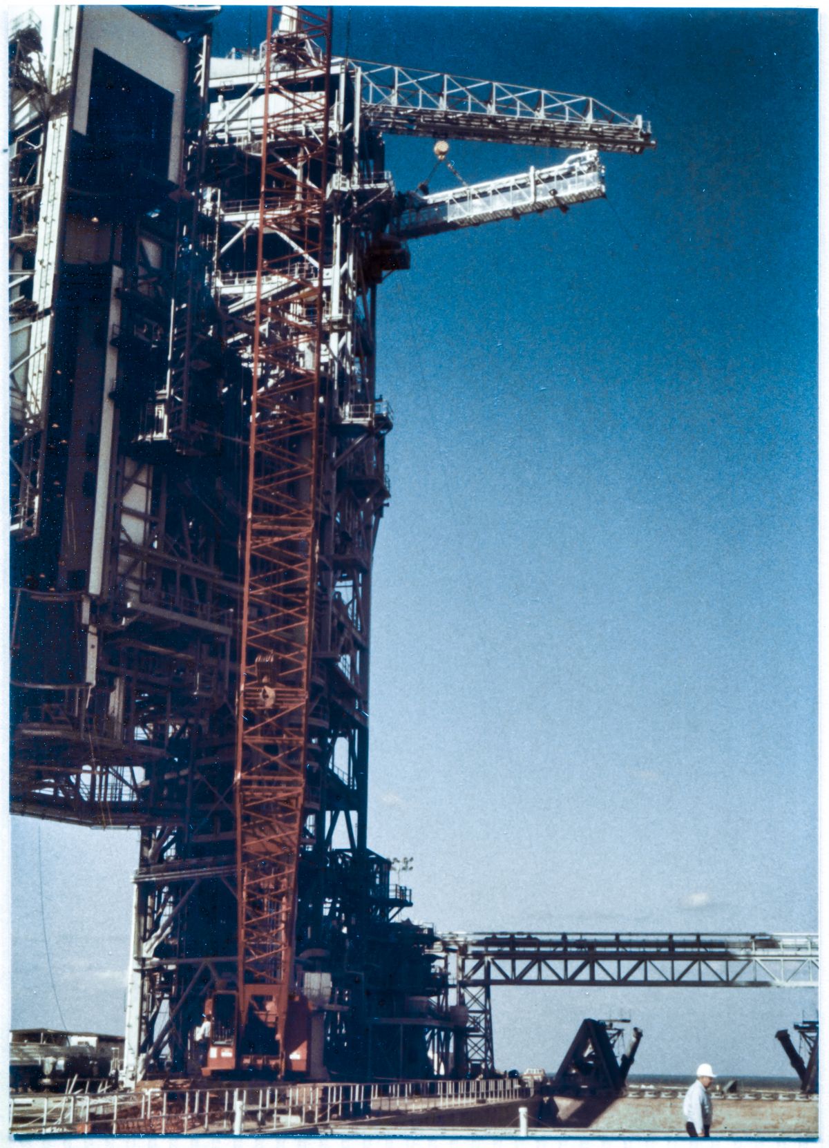 Image 109. At Space Shuttle Launch Complex 39-B, Kennedy Space Center, Florida, the GOX Arm has been lifted into its final position, and Ivey Steel's Union Ironworkers have commenced with bolt-up, fastening the Upper and Lower Hinge Boxes on the Arm to the Strongback which will support it, in its working location at the top of the FSS. The Hammerhead Crane, carrying the Lifting Sling which is still attached to the Arm, remains hooked-on, and will stay that way until the bolt-up is complete, at which point the Lifting Sling will be unpinned from the arm, and the Crane will swing to the side and lower it to the ground, where it will be removed from the hook and handed back over to NASA. Photo by James MacLaren.